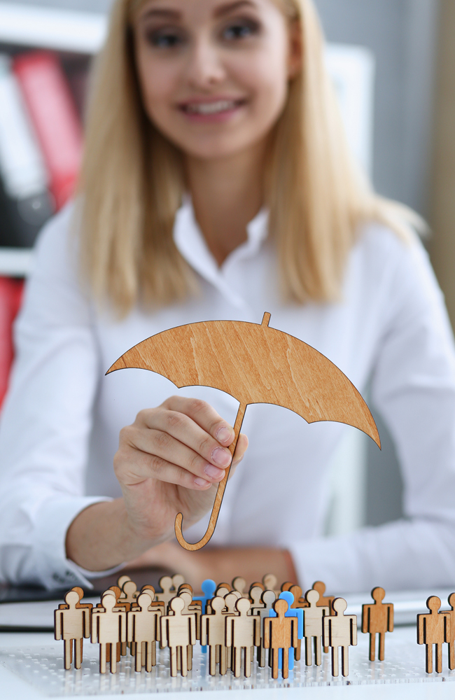 A financial agent holding a tiny umbrella over wooden cutouts that represent a family